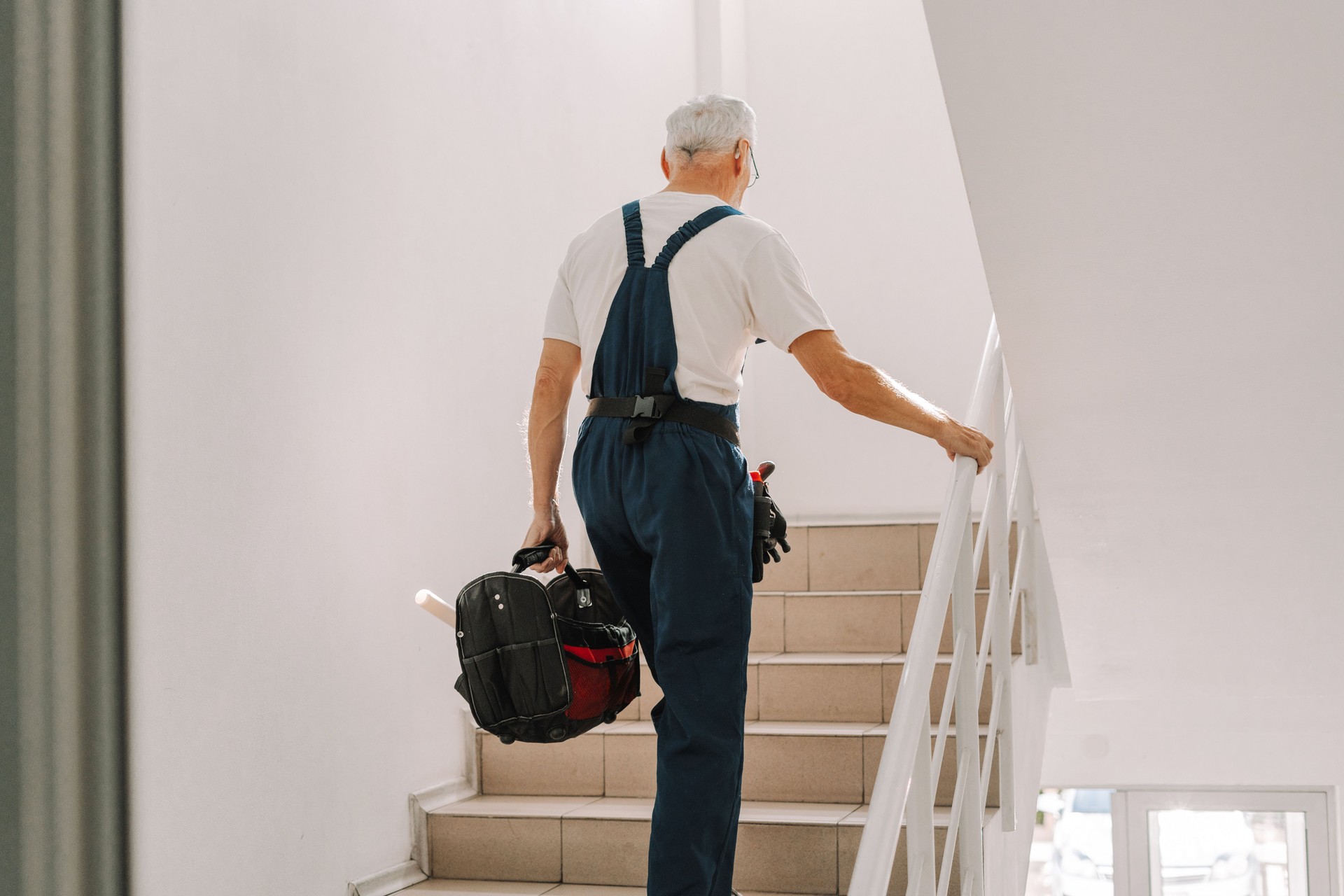Senior handyman walking up stairs holding tool bag at home